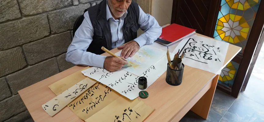 An older man seated at a desk writing Arabic script with a brush and ink