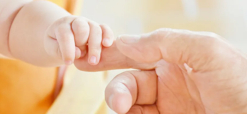 Eine Babyhand, die den Finger eines Erwachsenen umschließt, vor einem blassgelben Hintergrund
