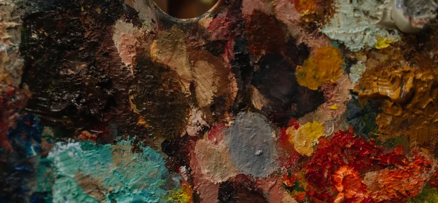 A close-up of an artist's palette covered in thick blobs of red, blue, yellow and white paint