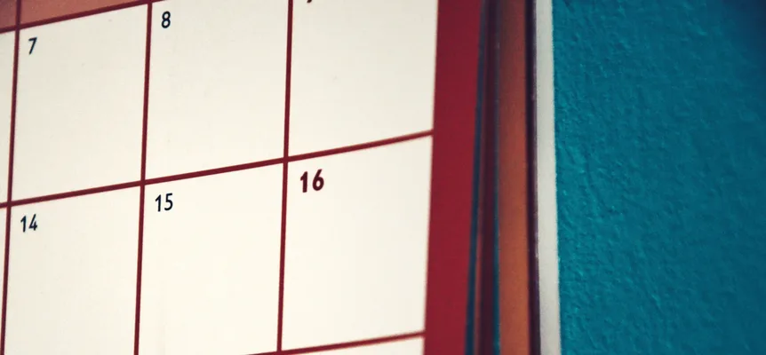 A plain white wall calendar hanging against a bright multicoloured painted wall
