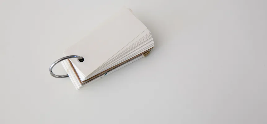 A small stack of blank white flashcards held together by a metal ring, lying on a pale grey surface