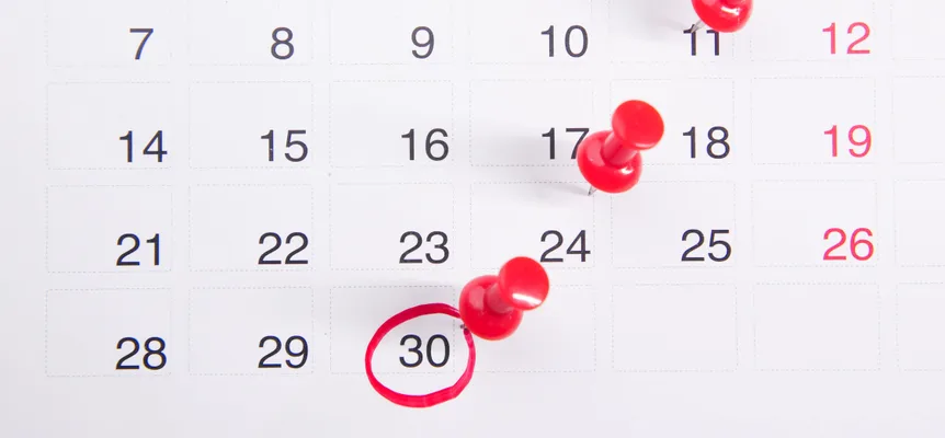 A wall calendar photographed close up, with red push pins stuck into several dates