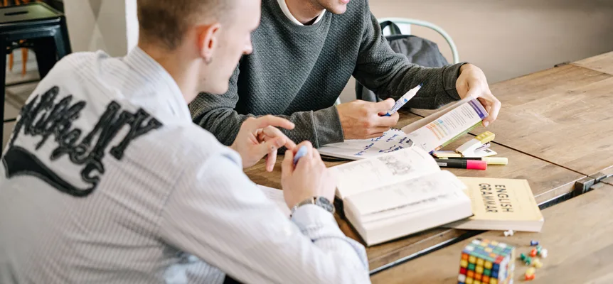 Two young men sitting side by side at a table, reading grammar books together