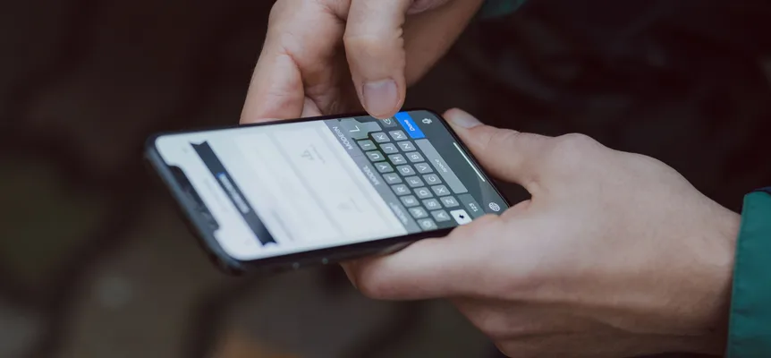 Two hands holding a smartphone sideways, one finger tapping a key on the on-screen English keyboard