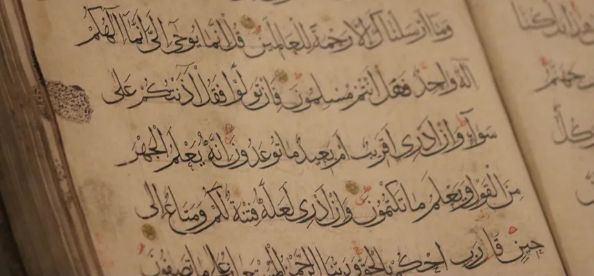 Close-up of an open handwritten Arabic manuscript page in black ink with red vowel marks and small gold circles between verses