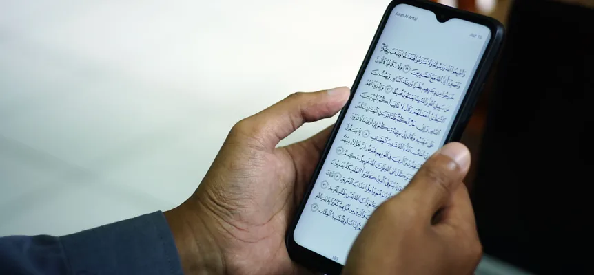 Zwei Hände halten ein Smartphone, das eine Seite des Korans in arabischer Schrift zeigt