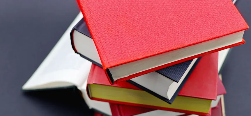 A pile of hardcover books with red, blue and yellow covers, stacked on a dark background