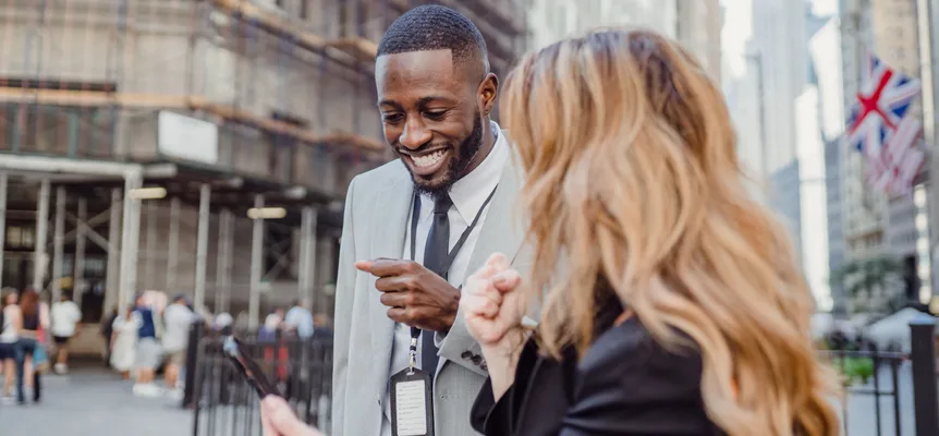 Two people standing on a city street, smiling and talking to each other