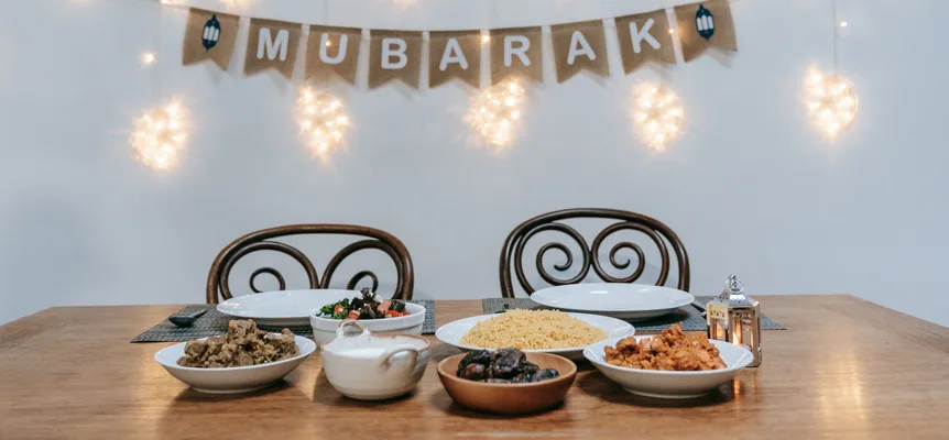A dinner table set with dates, rice and salads under a hanging Mubarak banner and glowing string lights