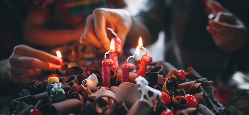 Hands lighting red glitter candles on a cake covered in chocolate curls, cherries and small toy animals