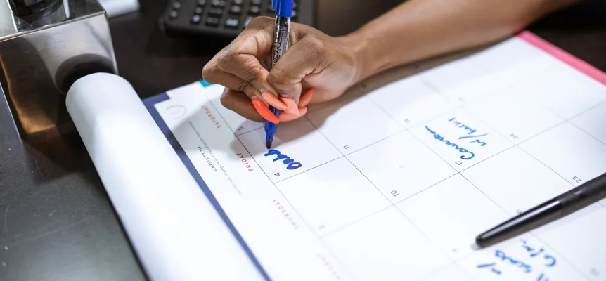 A hand writing on a wall calendar with a blue marker