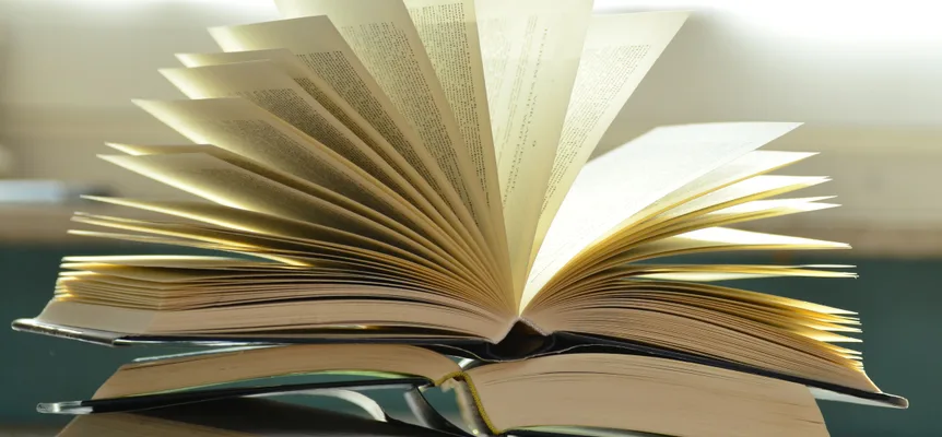A close-up of a stack of open books with their pages fanned out on a desk