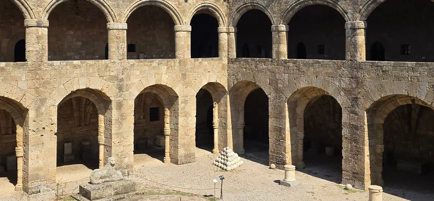 A historic stone courtyard ringed with arches under a clear blue sky