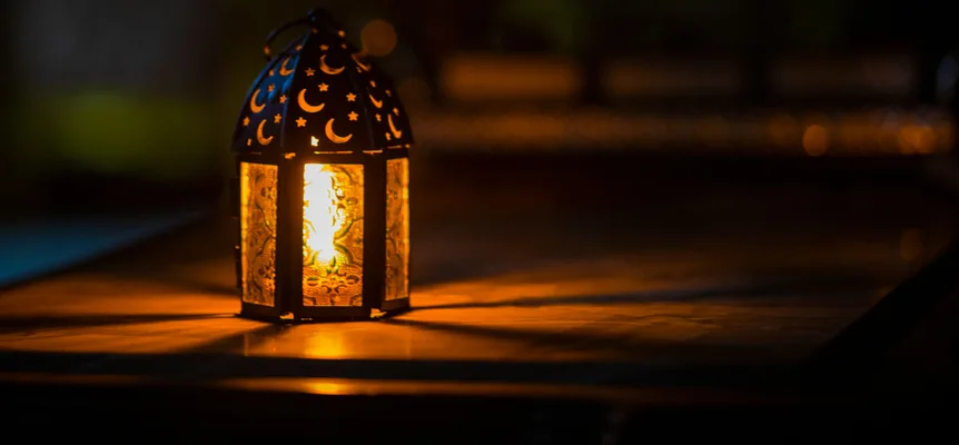 A metal lantern cut with crescent and star shapes glows with candlelight on a dark table